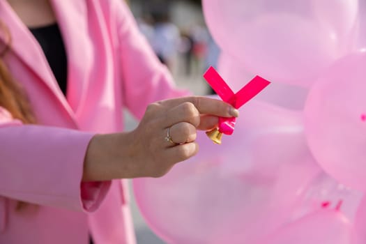 In the hand a pink ribbon against a background of pink balloons. Prevention of periodic breast examination.