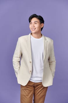 Smiling young Asian businessman in beige suit isolated on purple background