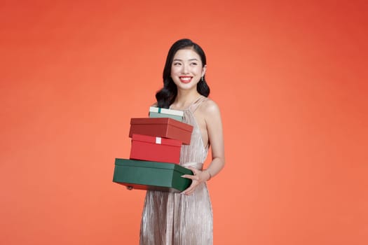Elegant young woman in glamorous dress holding wrapped gift box isolated on red