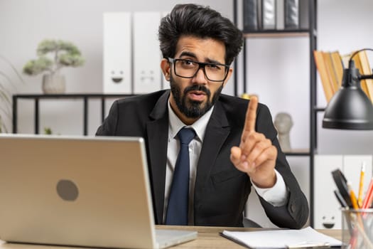 Business man working on laptop shakes finger, saying no, be careful, giving advice to avoid mistake