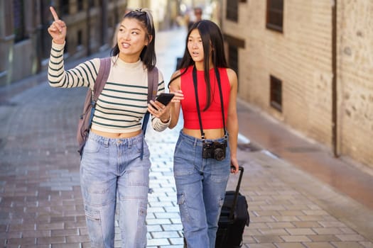 Asian female travelers pointing away while walking on street
