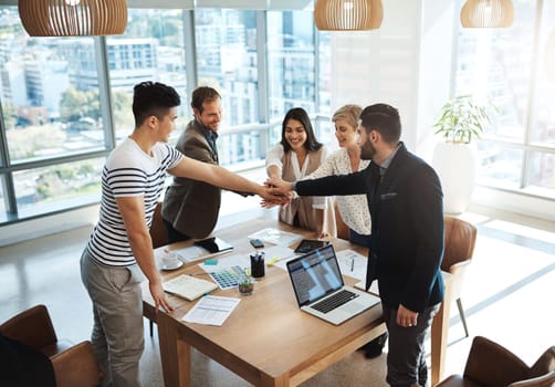 Together we can achieve greatness. a diverse group of businesspeople joining their hands in a huddle in an office.