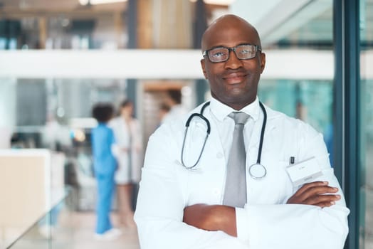 Your health is a serious subject around here. Portrait of a confident doctor working in a hospital with his colleagues in the background.