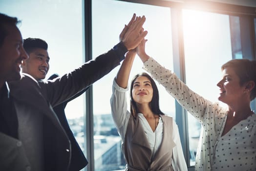 If we all cooperate, success will come easy. a diverse group of businesspeople high fiving in an office.