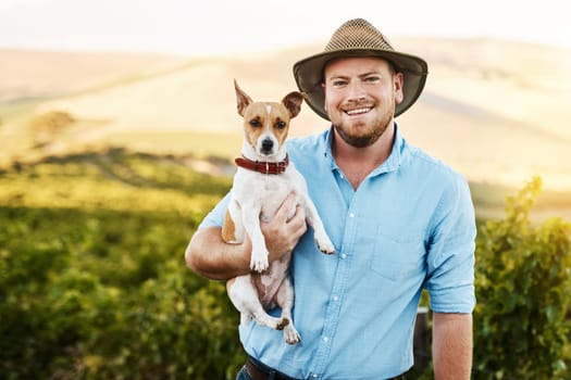 I cant go anywhere without this cute pup following me. Portrait of a farmer holding his dog in a vineyard.