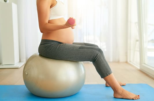Build a strong body, build a strong pregnancy. a pregnant woman working out with an exercise ball and weights at home.