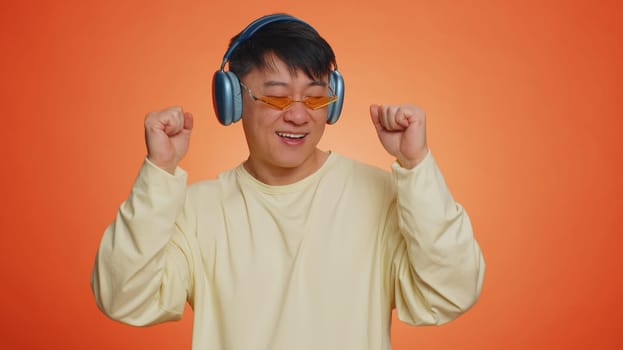 Asian happy man in headphones listening music dancing disco having fun relaxing on christmas party