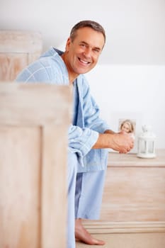 Smiling mature man in bathrobe sitting on bed. Portrait of a smiling mature man in bathrobe sitting on bed.