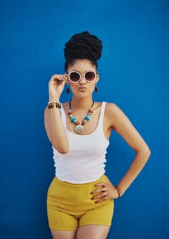 Facing the world with her funkiest look. an attractive young woman wearing funky sunglasses against a blue background.