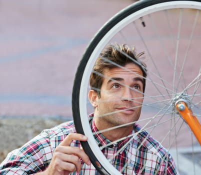 Doing some maintenance to ensure a smooth ride. a handsome man inspecting the wheel of his bicycle.