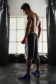 Hes dedicated to the sport of boxing. Full length shot of a handsome young boxer standing in the gym.
