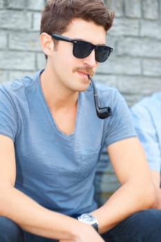 Doing everything with an individual style. Handsome young hipster smoking a pipe while sitting outdoors.