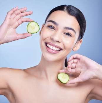 Studio Portrait of a beautiful mixed race woman holding cucumber slice. Hispanic model promoting the skin benefits of a healthy diet against a blue copyspace background