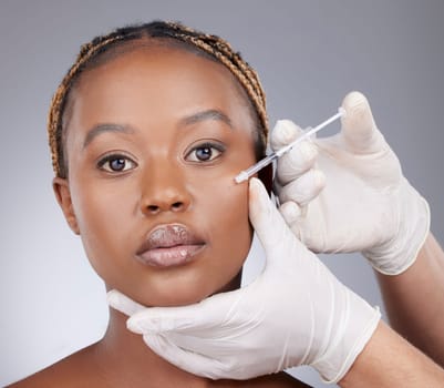 Im overcoming gravity. Studio shot of an attractive young woman getting her face injected by an unrecognizable surgeon against a grey background.