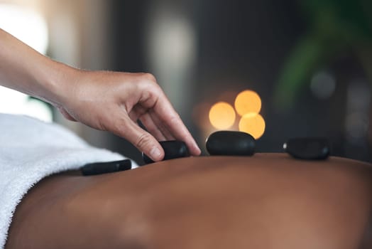 Hot stones are great for promoting deep relaxation. Closeups shot of an unrecognisable woman getting a hot stone massage at a spa.