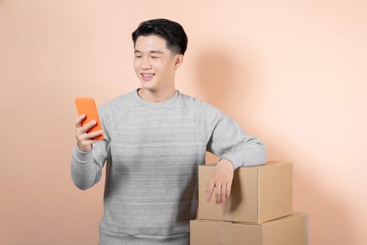 Asian delivery man using cellphone while standing with parcel boxes.