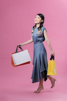 Attractive smiling Vietnamese woman wearing high heels and blue dress walking with paper-bags