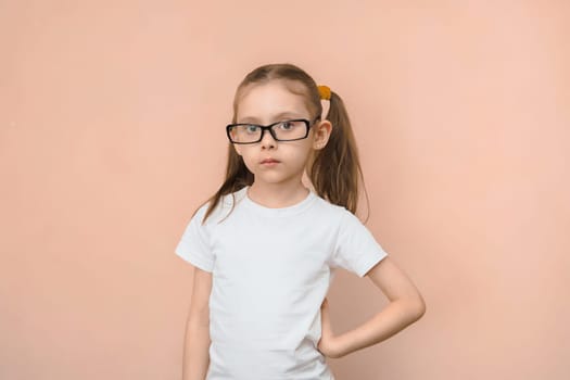 Portrait of a girl of elementary school age in rectangular optical glasses on a pink background