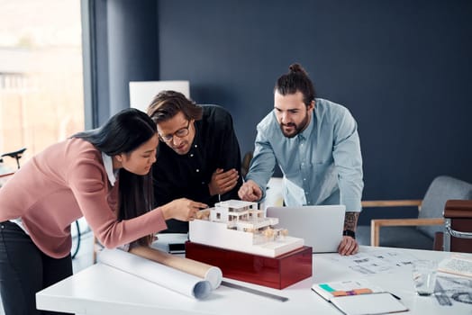 She always spots the tiniest of details. three young architects working on a scale model of a modern house in their office.