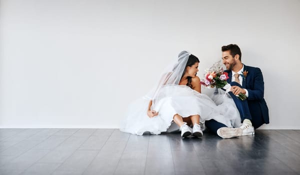 How excited are you. Studio shot of a newly married young couple sitting together on the floor against a gray background.