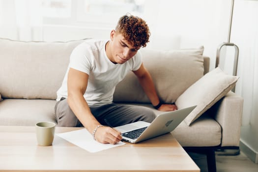 man interior sofa freelance browsing room wireless caucasian typing modern lifestyle laptop call male t-shirt blissful job laptop business
