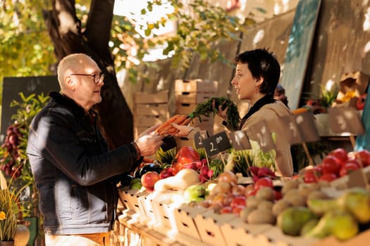 Woman seller showing organic natural carrots to elderly man