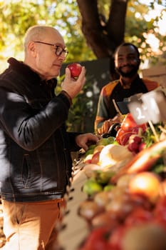 Retired man enjoying smell of fresh natural apples at farmers market