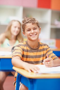 When you love school its easy to achieve. Friendly schoolboy sitting at his desk smiling happily at you - copyspace.