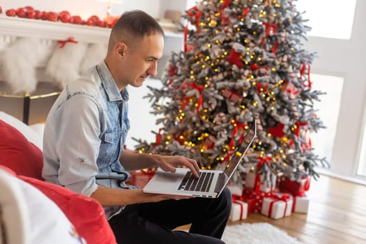 handsome man using laptop computer, talking on video chat call, shopping online. Christmas lights in the background