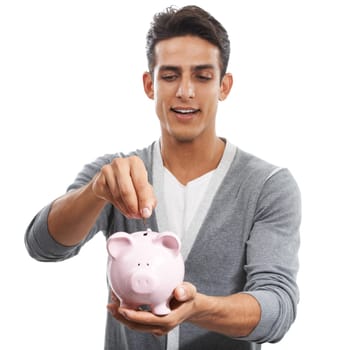 Saving for a rainy day. A handsome young man putting money into a piggybank against a white background.