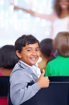 Eager young minds. Portrait of a young boy giving you the thumbs up while sitting in class.