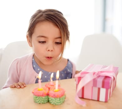Its my birthday. a young girl blowing out the candles on her birthday cupcakes.