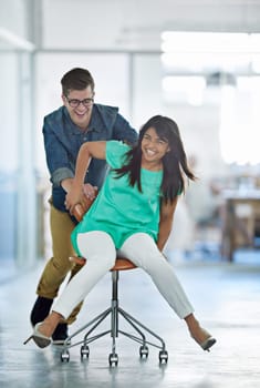 Office fun. a male coworker pushing his female coworker around an office in a chair.