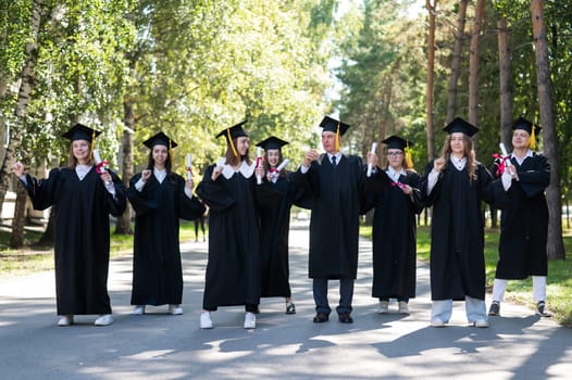Group of graduates in robes dancing outdoors. Elderly student.