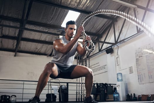 Health, gym and battle rope workout with man at a fitness center, cardio and muscle training. Power, energy and exercise by muscular athlete focused on intense movement, strength and endurance