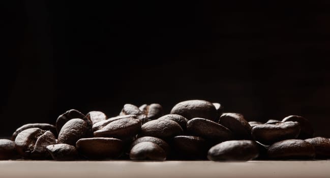 Experience love at first sip. Still life shot of coffee beans on a wooden countertop against a black background.