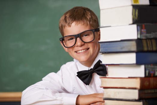This is any bookworms dream. A young boy wearing glasses and a bow-tie smiling at the camera from behind a stack of books.