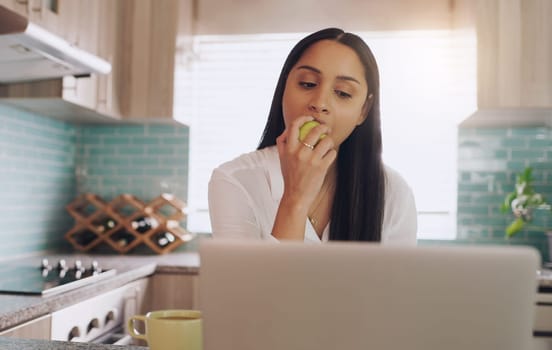 An apple a day keeps the illness at bay. a young woman eating an apple while she works at home.
