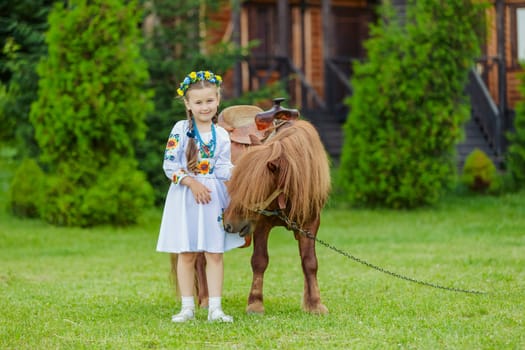 young girl in Ukrainian national dress strokes a pony