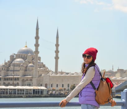 A young traveler with a backpack on her back looks at the camera in front of a mosque in Istanbul