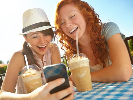 Jokes are made for sharing. Two adolescent girls enjoying smoothies while texting on a cellphone.