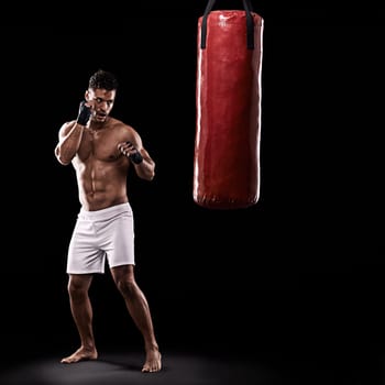 Never let your guard down. Studio shot of kick boxer working out with a punching bag against a black background.