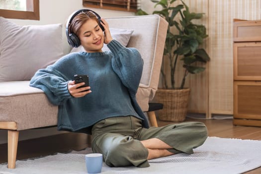 Happy asian woman listening to music from mobile phone while sitting near sofa at homes, Smiling girl relaxing with headphones in morning, Time to relax. copy space.
