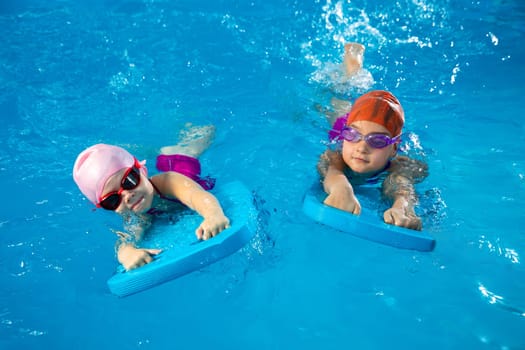 Two little kids learning how to swim in swimming pool using flutter boards