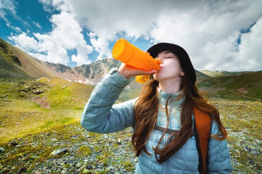 woman takes a break to drink from a water bottle while hiking. Young hiker drinks water in a mountain valley