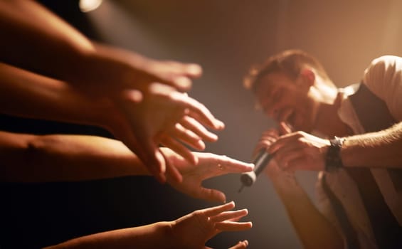 Hands, fans at concert and musician at music festival with microphone on stage with front row crowd. Audience, excited people reach for singer and live band performance in arena with energy at show.