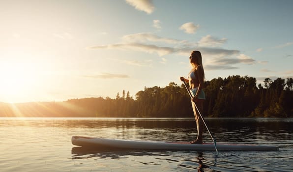 Today is a great day to go paddle boarding. an attractive young woman paddle boarding on a lake.
