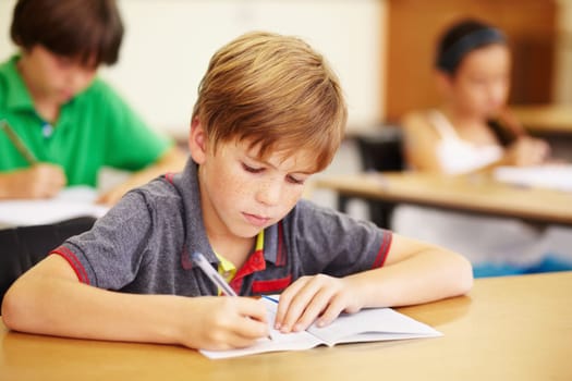 Boy kid, school classroom and writing test with focus, concentration and thinking for education goals. Male child, book and pen in class for assessment, studying or learning at desk for scholarship.