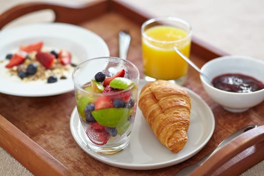 Nutritious and delicious. Closeup of a breakfast tray with juice, fruits salad, a croissant and muesli.