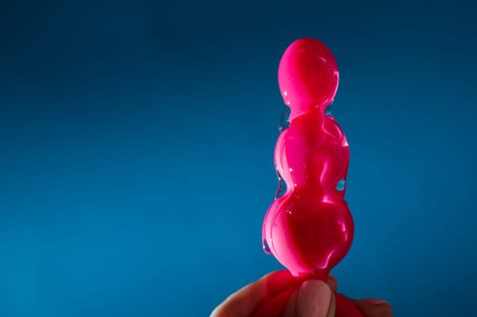 Woman pouring lubricant on pink anal beads on blue background.